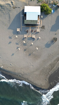 Aerial view of Ada Bojana beach with a small building, wooden walkways, and sun umbrellas on the sand in Ulcinj Municipality, Montenegro.