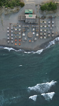 Aerial view of Ada Bojana beach resort with wooden structures, rows of beach umbrellas, and sandy shoreline meeting the dark sea in Ulcinj Municipality, Montenegro.