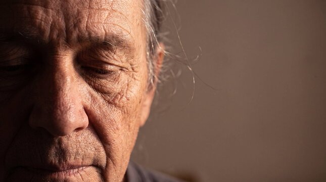 Close up portrait of elderly person's weathered face with eyes closed in dramatic light