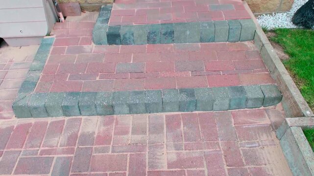 New Mono Driveway step. Red and gray mono block pavers form elegant steps. Each step leads toward a front door. Pavers show natural texture and color variation. Step edges are smooth and well-defined