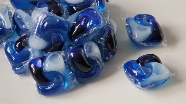 Pile of blue laundry detergent pods in clear packaging on a white surface