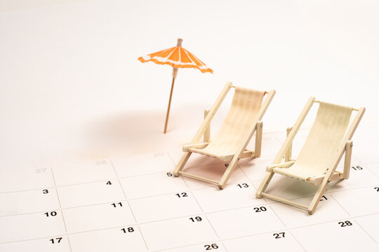 Planning summer vacation, beach holiday getaway, marking dates on calendar with mini deck chairs and umbrella