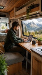 Obraz premium Man working on a laptop inside a wooden camper van with panoramic window showing mountains and lake view