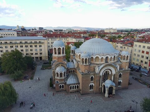 Aerial view of the Church of the Holy Seven Saints with its domes and brick architecture surrounded by urban buildings and a paved square in Sofia, Sofia City Province, Bulgaria.
