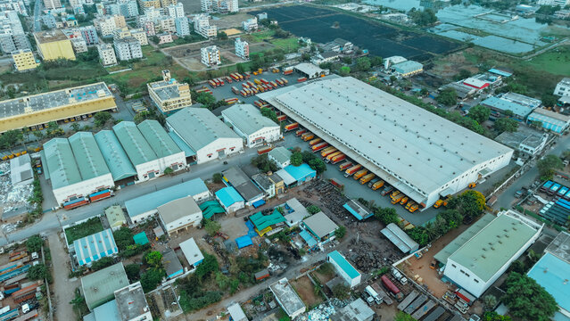 Aerial view of a logistics facility with numerous trucks parked at loading docks, surrounded by industrial buildings and warehouses in India.