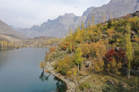 Aerial view of Shangrila Resort and Kachura Lake surrounded by vibrant autumn foliage, rocky mountains, and calm blue water in Skardu, Pakistan.