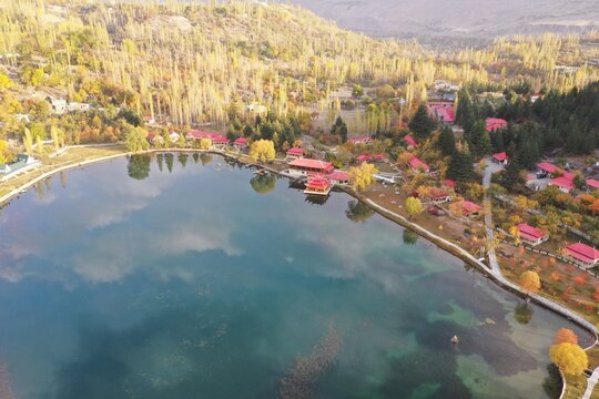 Aerial view of Shangrila Resort and Kachura Valley in the autumn season, featuring vibrant yellow trees, red-roofed buildings, and the calm blue waters of Lower Kachura Lake in Skardu, Pakistan.