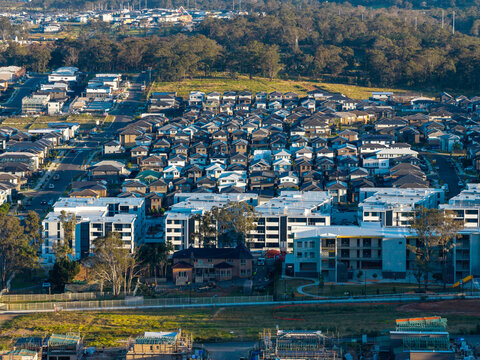 Aerial view of a modern suburban housing estate featuring rows of houses and apartment buildings surrounded by trees and ongoing construction in Tallawong, New South Wales, Australia.
