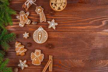 Fototapeta premium Gingerbread cookies shaped like a man, angel, and ornament arranged on a wooden table with cinnamon sticks, sugar cubes, and pine branches for a festive holiday setting