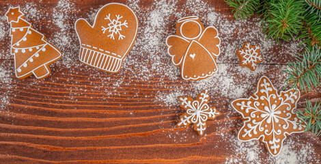Fototapeta premium Gingerbread cookies shaped like Christmas tree, mitten, angel, snowflake, and star arranged on wooden table with powdered sugar and pine branches