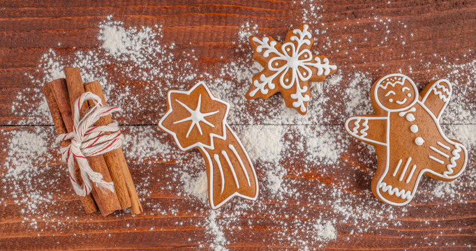 Gingerbread cookies shaped like a star, snowflake, and gingerbread man arranged on a wooden surface with cinnamon sticks and powdered sugar decoration