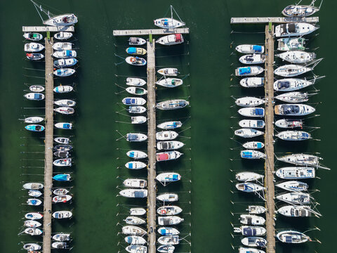 Aerial view of Bonnerup marina with numerous sailboats and motorboats moored in orderly rows along wooden piers in the calm green water of Bonnerup, Denmark.