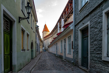 Fototapeta premium Charming morning view of Laboratooriumi street in Tallinn. Empty medieval cobblestone alley along the ancient fortress wall and historic tower under a soft sky in Old Town, Estonia.