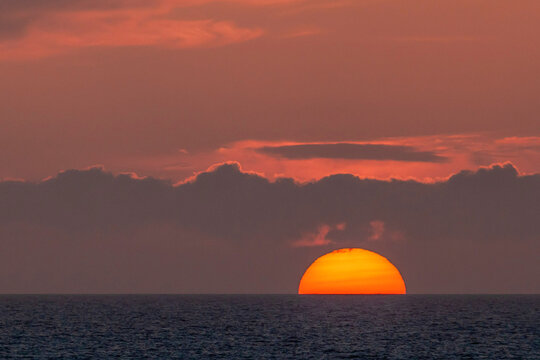 Amazing orange sunset over the sea. Scenic minimalist seascape with a large sun disk half down the water horizon under dramatic pink twilight clouds in Europe.