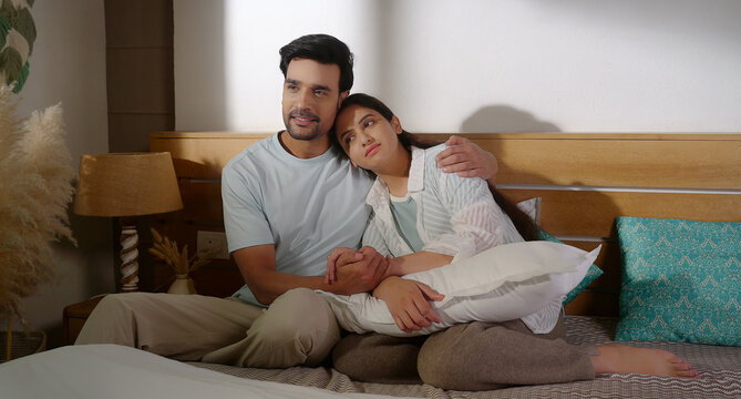 Indian young adult gen z male female pair couple sitting cozy bed hold hand do patch up share love care happy man woman talk speak take rest on shoulder spend time enjoy indoor room place