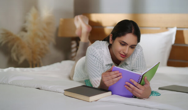 Indian young adult gen z relax calm woman lying on cozy bed read new novel book story indoor room resting girl spend free time do self care enjoy day take break from job work home place