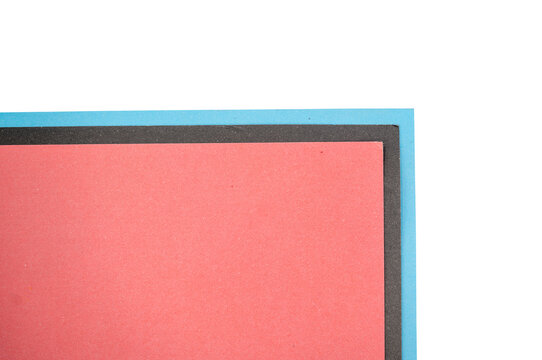 Abstract close-up of layered red, blue, and dark rectangular paper shapes against black, creating a bold minimalist geometric composition with subtle texture and strong color contrast.