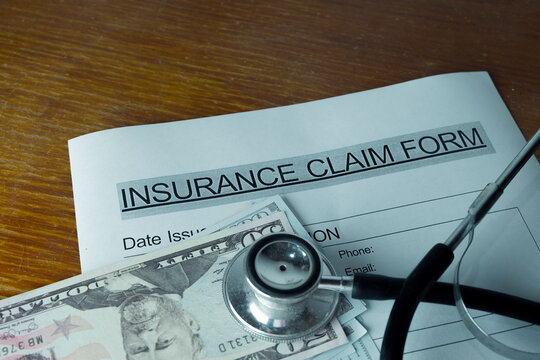 Close up of a stethoscope and US dollar bills resting on a health insurance claim form. Concept of medical billing, healthcare costs, expensive treatment, and life insurance payout.