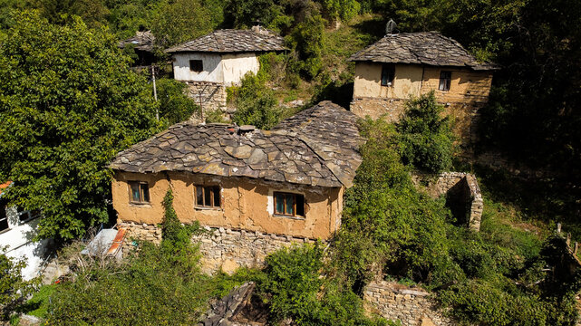 Aerial view of traditional stone houses with slate roofs and mud-brick walls nestled in the lush greenery of the historic village of Gostusa, Pirot District, Serbia.