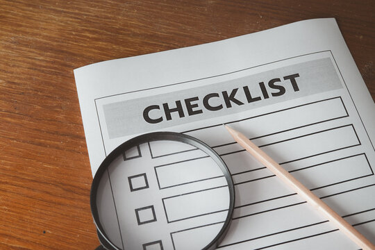 Close up of a blank checklist form with a magnifying glass and a wooden pencil on a wooden desk. Concept of quality control, business inspection, auditing, goal setting, and task management.