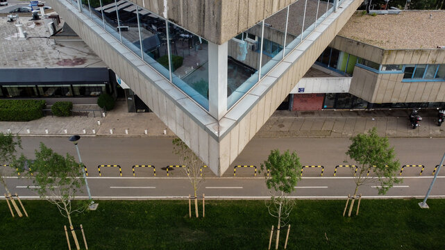 Aerial view of the brutalist Sportski centar 25. maj with its sharp concrete corner and glass facade overlooking a street with bollards and young trees in Beograd, Grad Beograd, Serbia.