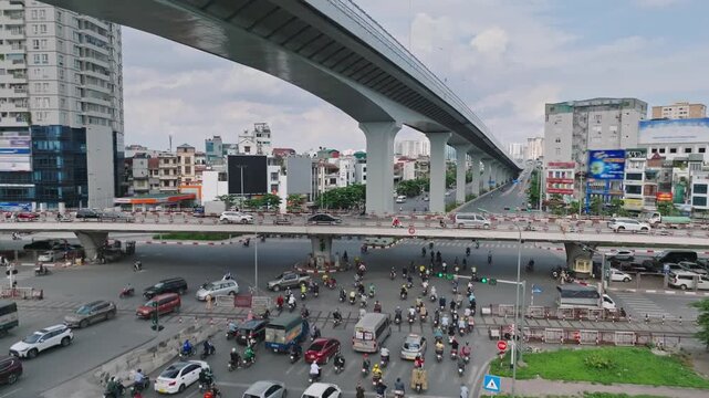 Busy urban traffic flows beneath Hanoi's elevated Ring Road 3 on Giai Phong Street, featuring motorcycles, cars, city buildings, and modern transportation infrastructure.