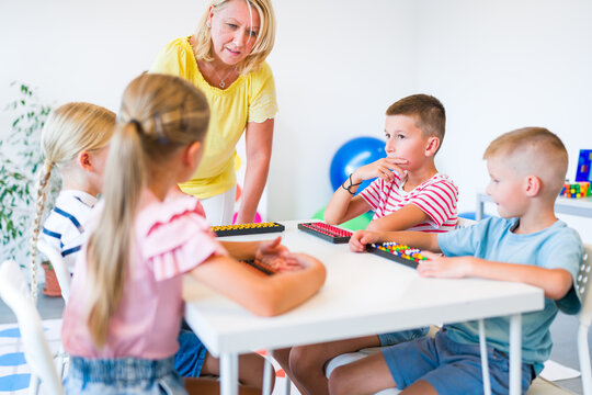 Group of children practicing mental arithmetic and counting with abacuses during a lesson with their teacher in a classroom.