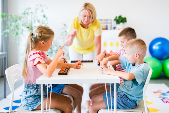 Group of children practicing mental arithmetic and counting with abacuses during a lesson with their teacher in a classroom.