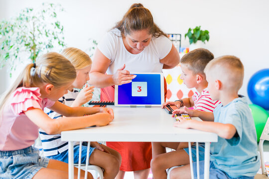 Teacher guides children practicing mental arithmetic and calculations with abacuses using a digital learning app during a classroom lesson.