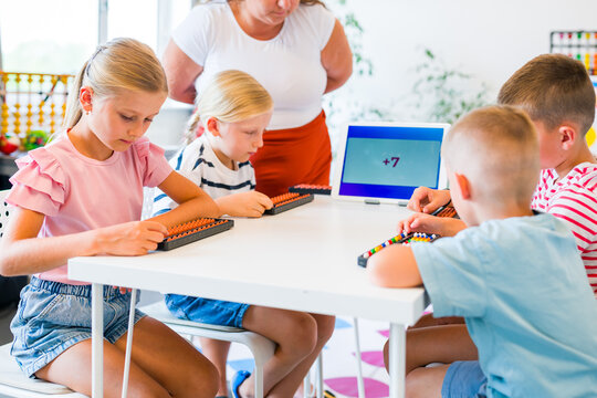 Teacher guides children practicing mental arithmetic and calculations with abacuses using a digital learning app during a classroom lesson.