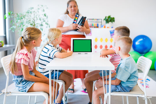 Teacher guides children practicing mental arithmetic and calculations with abacuses using a digital learning app during a classroom lesson.