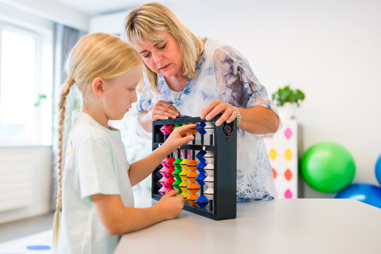 Teacher helps a young boy learn mental arithmetic and counting using a large colorful abacus during an educational lesson.