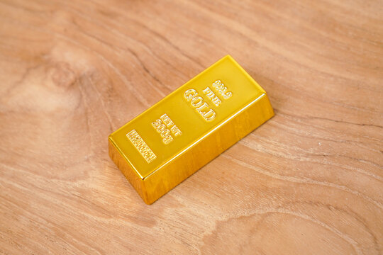 A gleaming gold bar rests on a wooden background.