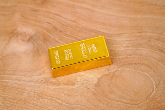 A gleaming gold bar rests on a wooden background.