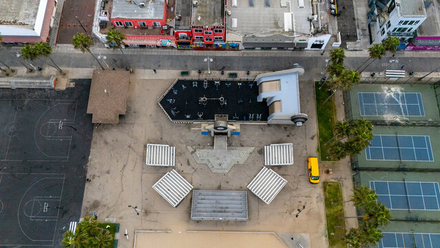 Aerial view of the Muscle Beach outdoor gym at Venice Beach, featuring weightlifting equipment, tennis courts, palm trees, and the boardwalk in Los Angeles, California, United States.
