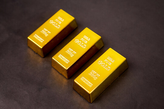 Three polished gold bars gleam softly against a dark background. Each bar bears engraved markings, indicating purity and weight. They rest in a diagonal line, creating a sense of balance and value