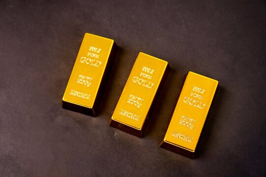 Three polished gold bars gleam softly against a dark background. Each bar bears engraved markings, indicating purity and weight. They rest in a diagonal line, creating a sense of balance and value