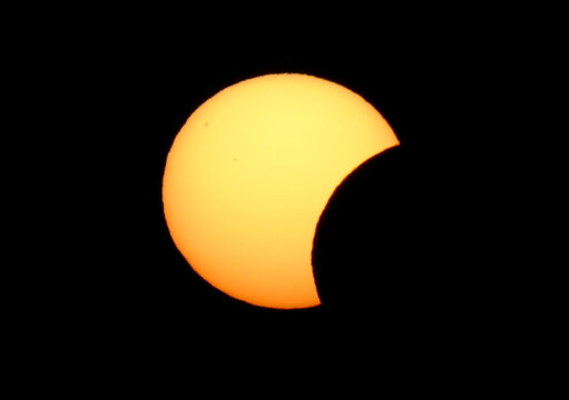 Crisp telephoto close-up of a partial solar eclipse against a pure black sky, featuring visible sunspots and a clear, detailed solar disk.