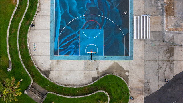 Aerial view of the artistic blue basketball court at Venice Beach with concrete surroundings and bleachers in Los Angeles, California, United States.