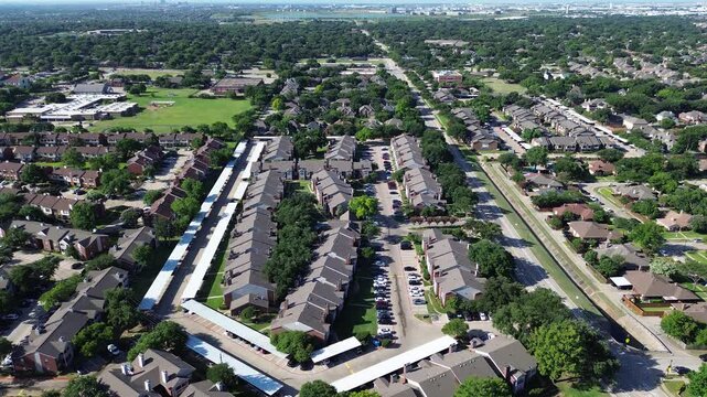 Multifamily residential buildings align beside Parkway Boulevard near Mockingbird Elementary School. White covered carports, paved parking courts, lush mature trees populate Coppell, Texas.