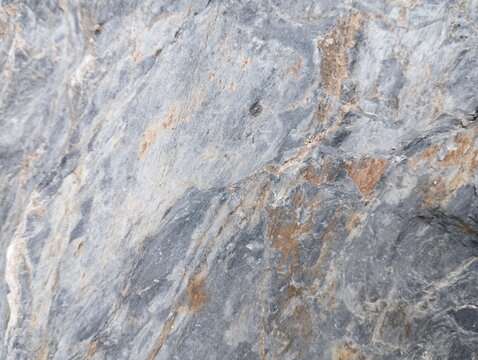 Raw stone background with smooth-yet-rough texture, cool gray base with warm brown and rust-colored veins. Natural mineral pattern, slate or granite material, authentic geological backdrop.