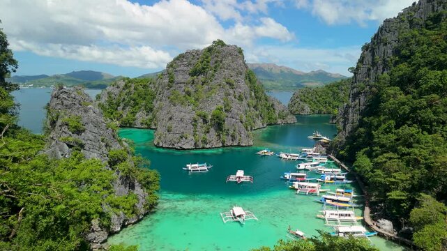 Stunning aerial view of turquoise waters in Kayangan lake Coron Palawan with traditional Filipino outrigger boats docked at cliff base.