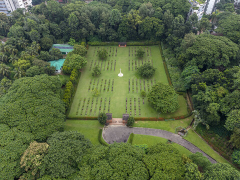 Aerial view of Chittagong War Cemetery with rows of graves, a central monument, and lush green trees surrounding the site in Chittagong, Chittagong Division, Bangladesh.