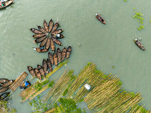 Aerial view of Sadarghat with numerous wooden boats arranged in a circular pattern on the river, surrounded by bamboo poles and aquatic vegetation in Dhaka, Dhaka Division, Bangladesh.