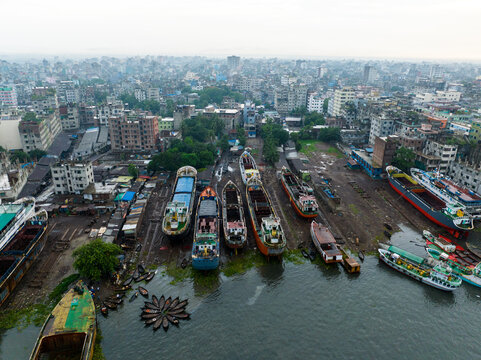 Aerial view of Sadarghat river port in Dhaka featuring cargo ships docked for maintenance along the riverbank with a dense urban skyline, Dhaka, Dhaka Division, Bangladesh.