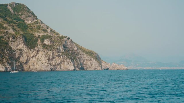 Rocky cape tapering into the sea with a distant Amalfi coast