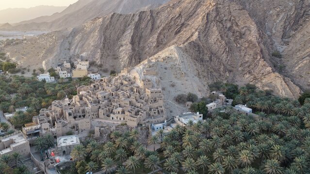 Aerial view of the historic Birkat Al Mouz ruins nestled against rugged mountains, surrounded by lush date palm plantations in Birkat Al Mouz, Ad Dakhiliyah, Oman.