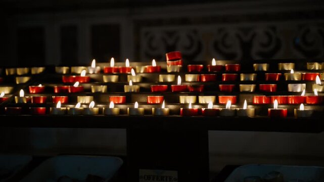 Rows of votive candles glowing in a dark church interior