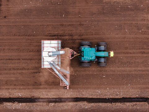 Aerial view of a tractor operating a pneumatic vacuum harvester on a peat bog, showcasing industrial peat mining and soil substrate extraction, Talsu novads, Latvia.