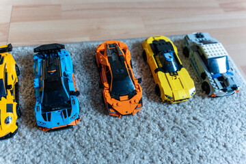 Obraz premium Warsaw, Poland - Sep 4, 2026: Row of five LEGO Technic model cars in yellow, orange and blue on a gray rug